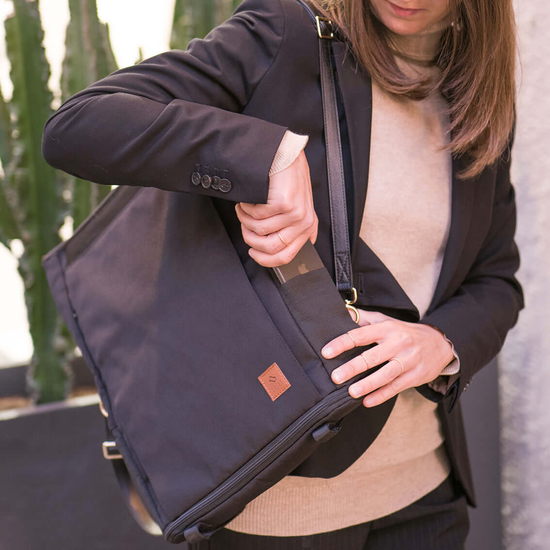 Woman takes out her smartphone from the side pocket of her black convertible backpack